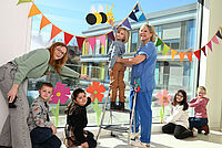 Frühlingsgeschenk von Kindern für Kinder Niklas, Amara, Matilda, Leyla und Greta (v.l.n.r.) kleben mit OGS-Leiterin Kareen Winzker und Kinderkrankenschwester Sandra Kuhse frühlkingshaften Fensterschmuck an eine große Fensterscheibe des Kinderzentrums.