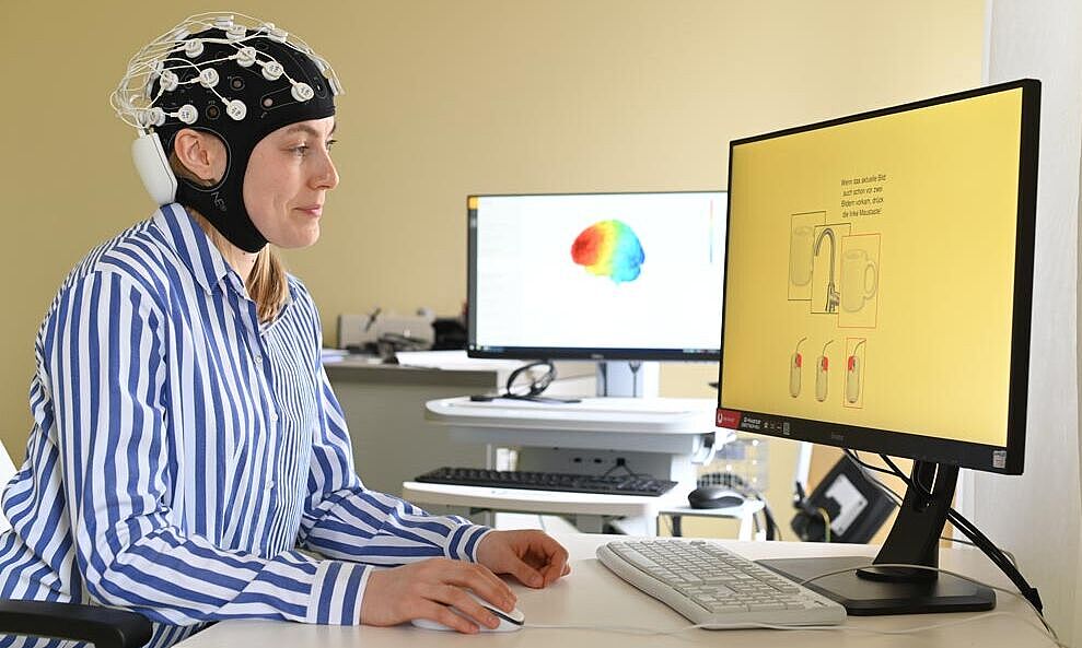 Forschung in der Kinder und Jugendpsychiatrie Mädchen sitzt mit einer Mütze an der Elektroden befestigt sind vor einem Bildschirm.