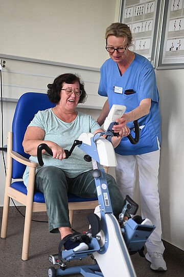 Schmerztherapie im EvKB. Eine Pflegekraft unterstützt eine Patientin bei der Verwendung von von einem Sportgerät.